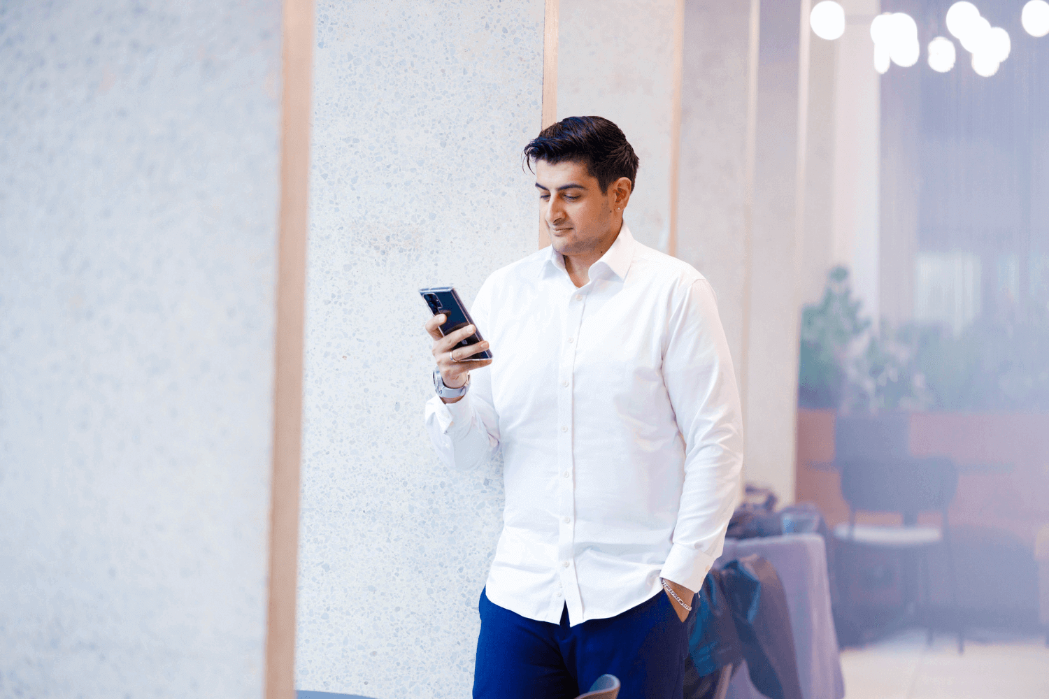 A man looking at his mobile phone while leaning against a pillar.