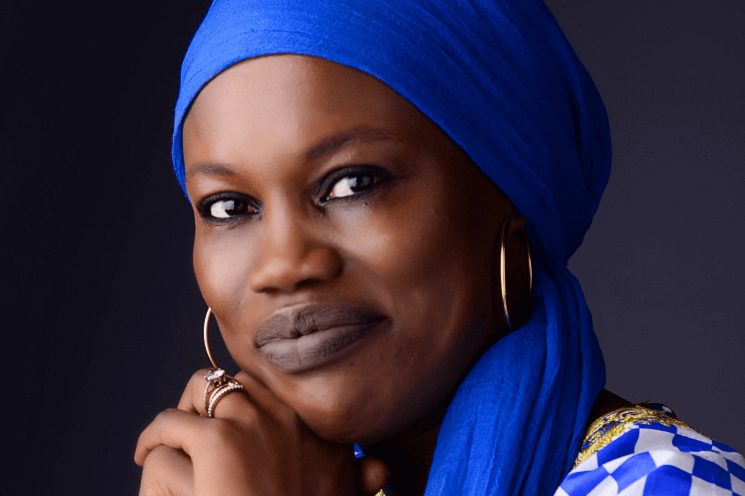 A woman resting her head on her hands She is wearing a blue and white checked top and a royal blue head covering. 