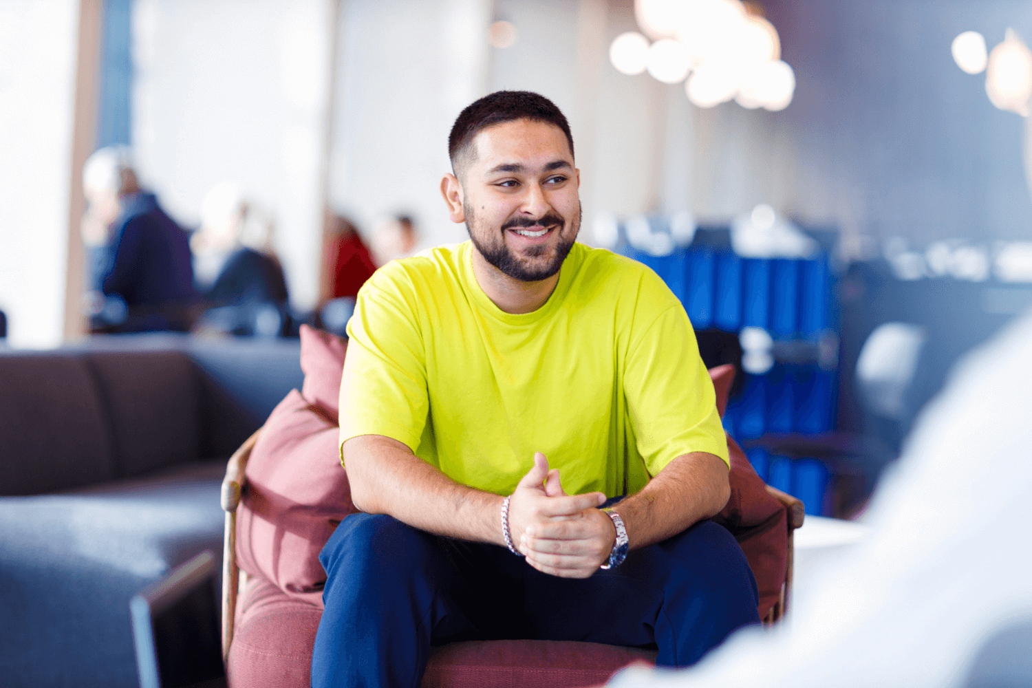 Um jovem com uma camiseta amarela, sorrindo para os colegas ao lado.