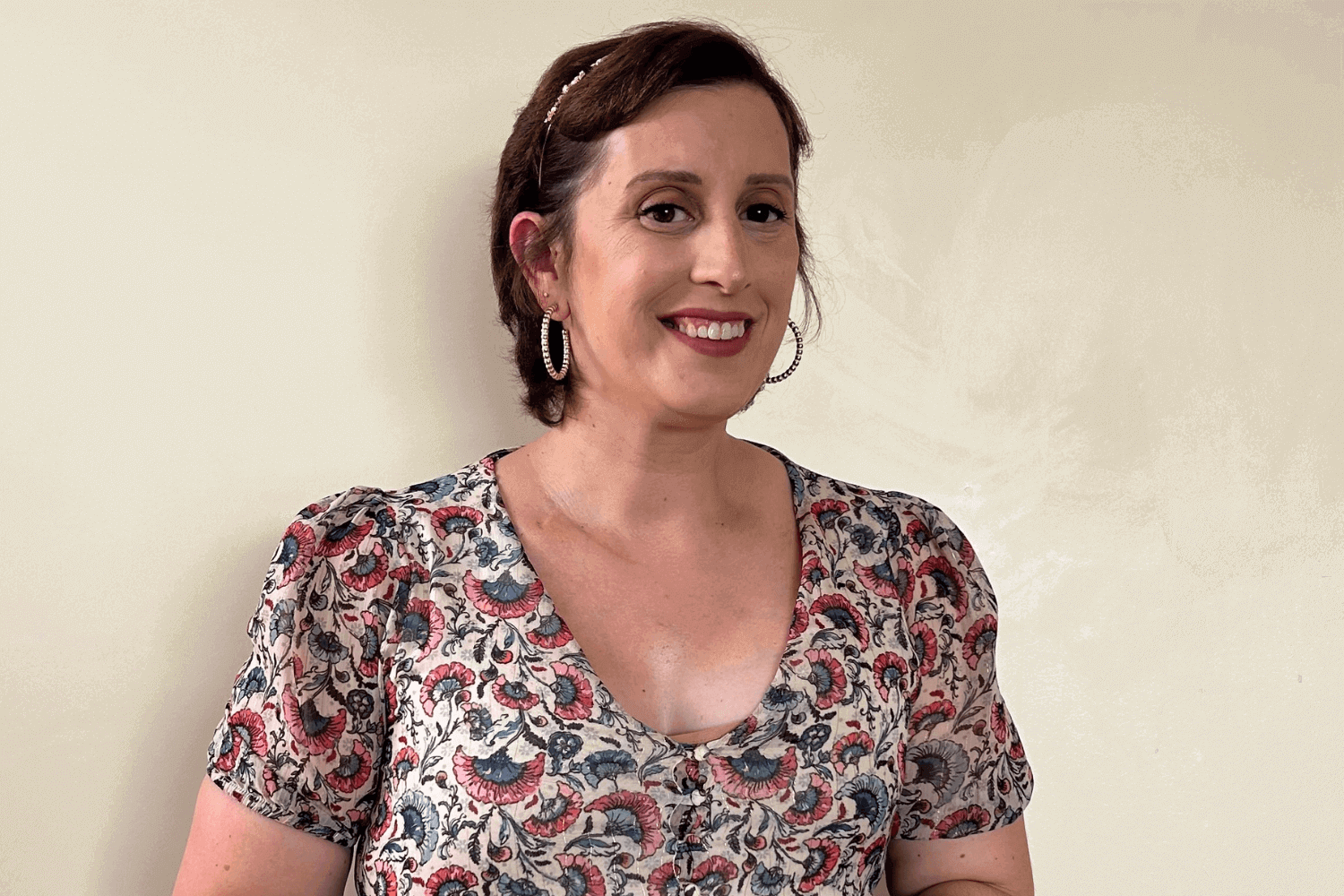 Uma mulher com cabelo castanho curto e brincos de argola dourados. Veste um top multicolorido com padrões. 