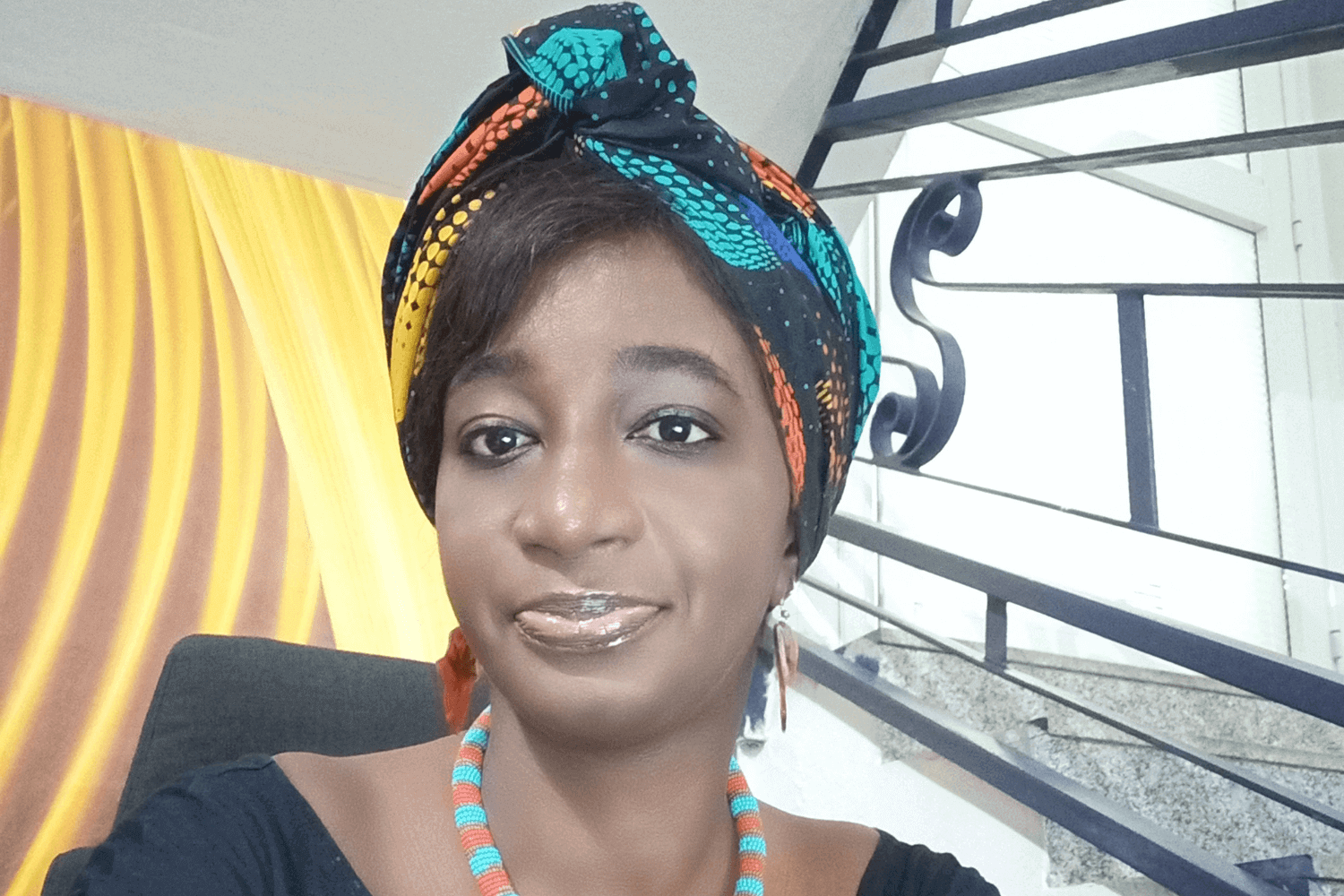 Uma mulher com um top azul e um lenço multicolorido na cabeça. 