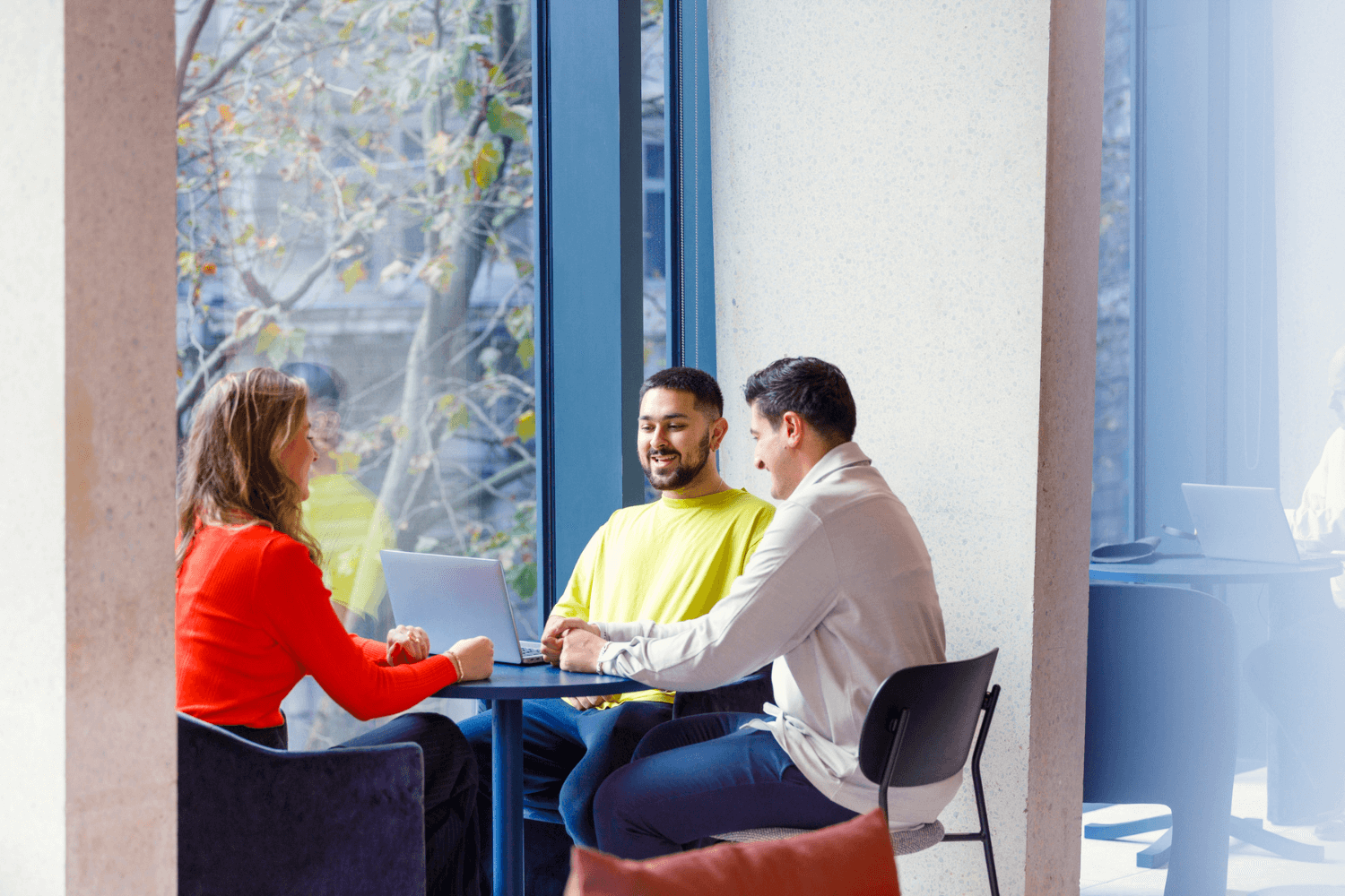 Eine Gruppe von drei Hochschulabsolventen arbeitet gemeinsam an einem Tisch am Fenster.