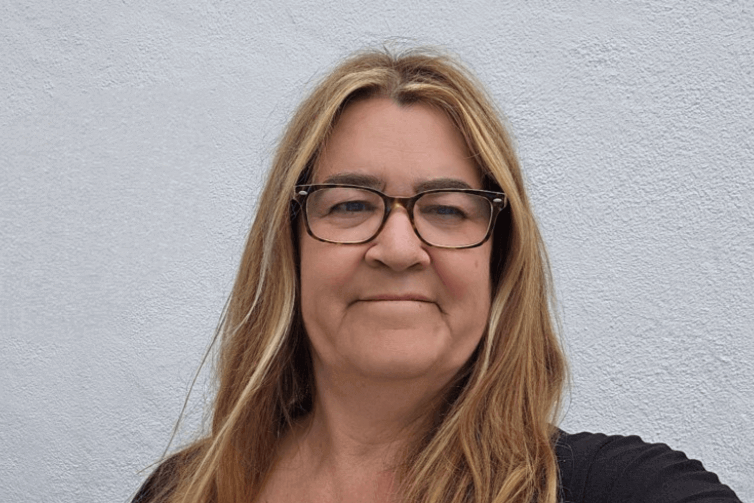 Eine Frau mit langen Haaren und Brille. Sie hat ein schwarzes Oberteil an.