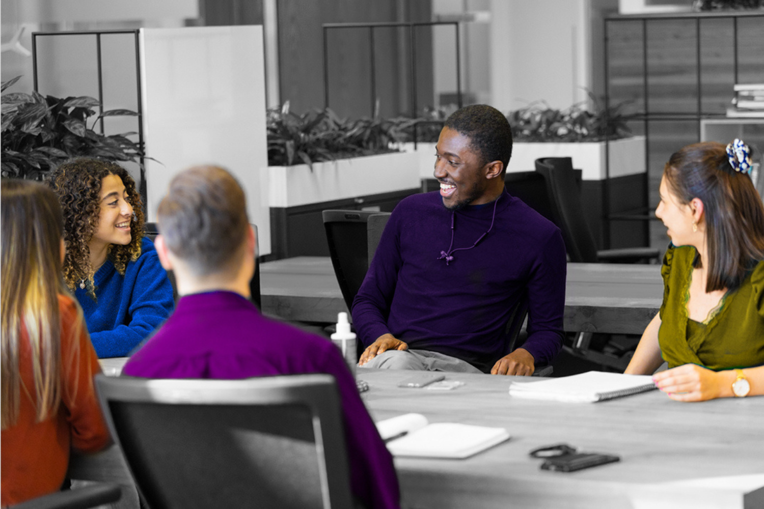 Imagen en blanco y negro, en la que sólo la ropa y el tono de la piel aparecen en color. Esta foto muestra a cuatro jóvenes trabajando juntos en una reunión abierta.