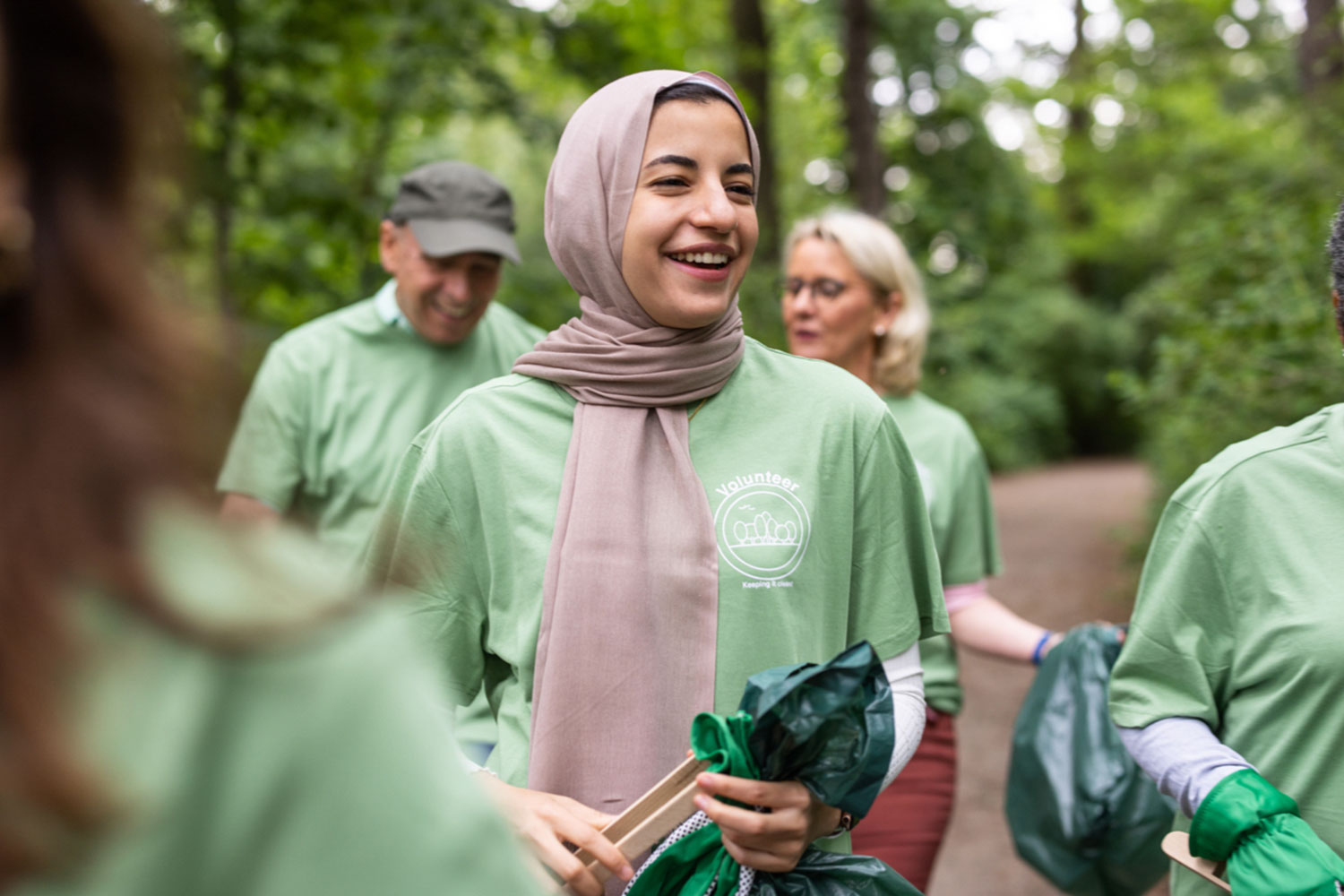 Mujer con pañuelo en la cabeza, camiseta verde y bolsa de basura.