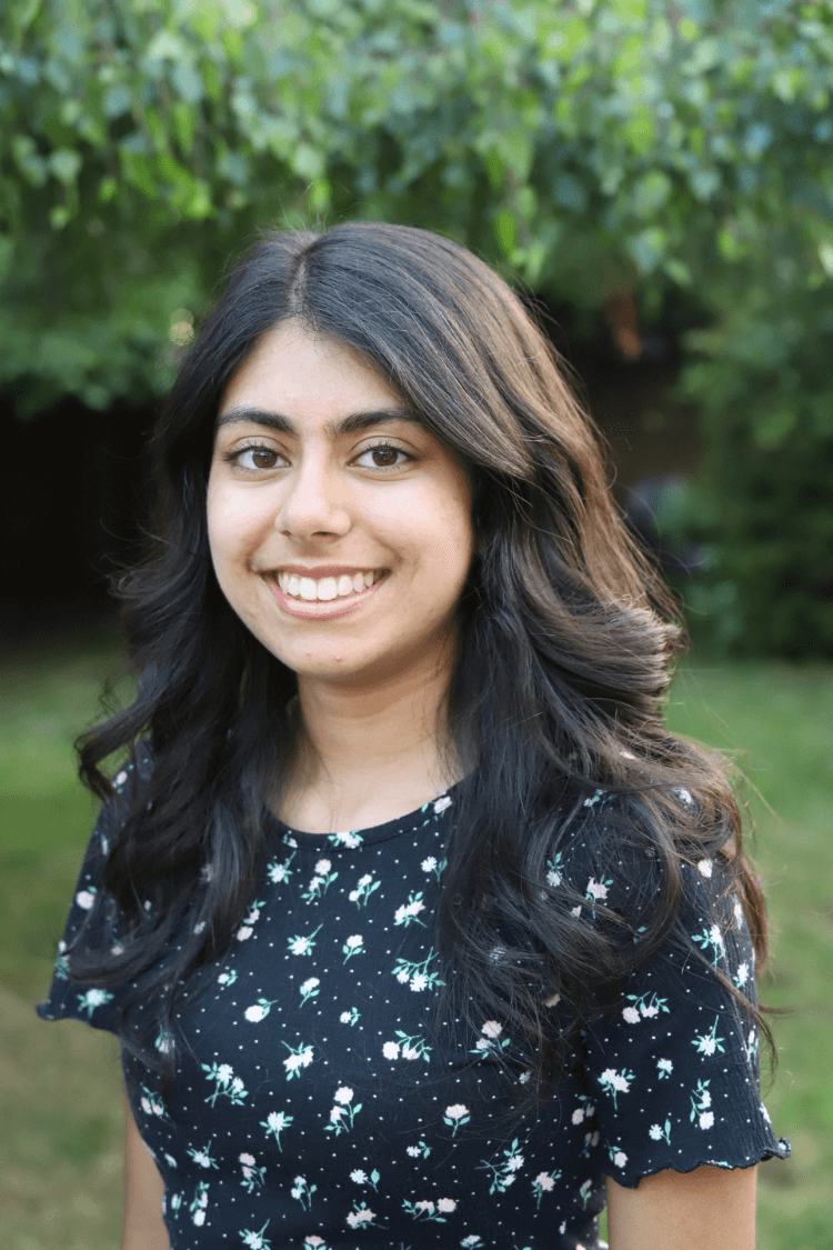 Una mujer joven con el pelo largo y castaño. Lleva una blusa azul de manga corta con detalles florales. 