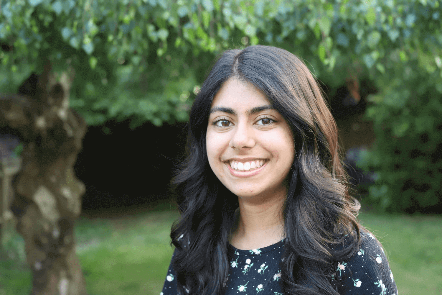 Una mujer joven con el pelo largo y castaño. Lleva una blusa azul de manga corta con detalles florales. 