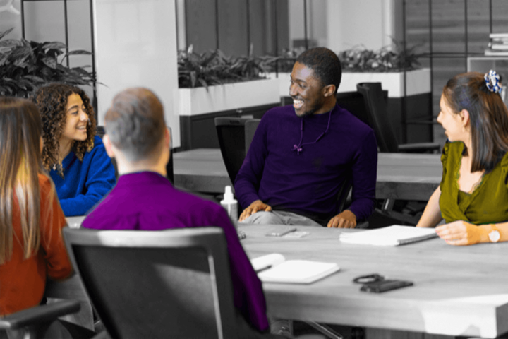 Image en noir et blanc, seuls les vêtements et le teint de la peau sont en couleur. Un groupe de cinq jeunes travaille ensemble.