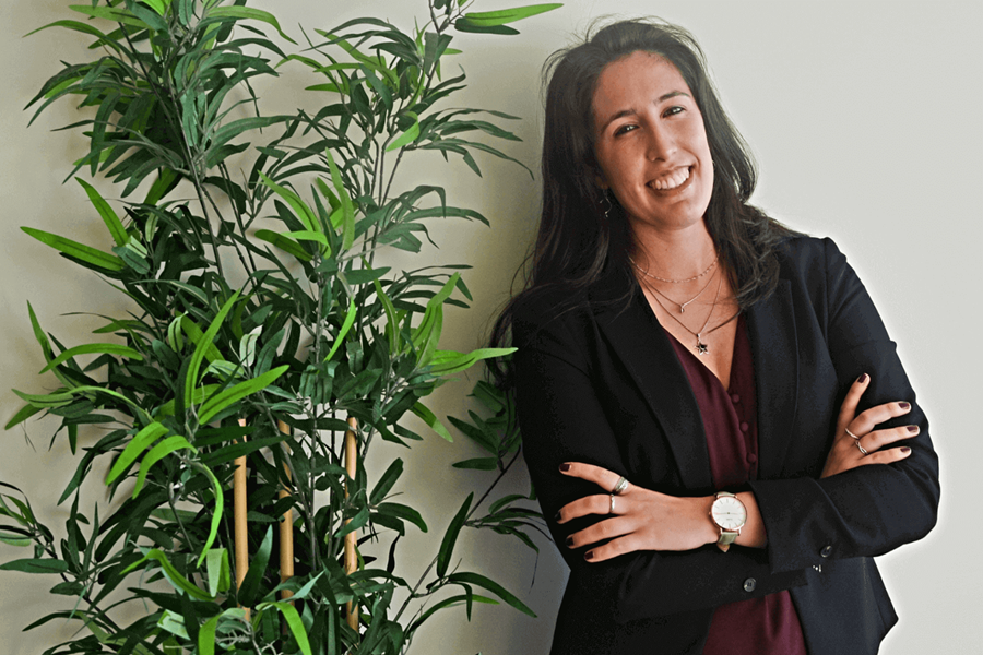 Une femme se penche à côté d'une plante. Elle a de longs cheveux bruns et porte une veste noire et une robe rouge.