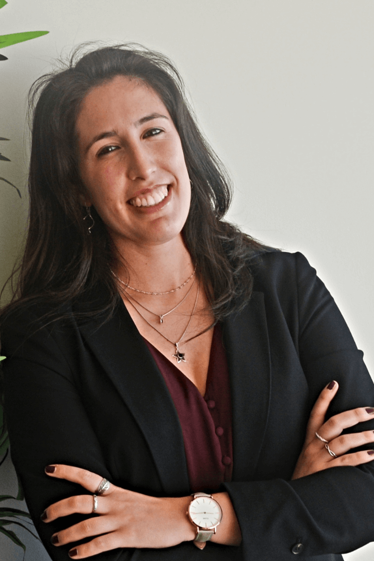 Une femme se penche à côté d'une plante. Elle a de longs cheveux bruns et porte une veste noire et une robe rouge.