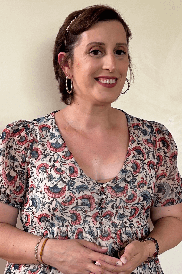 Une femme aux cheveux bruns courts et aux boucles d'oreilles dorées. Elle porte un haut multicolore à motifs.