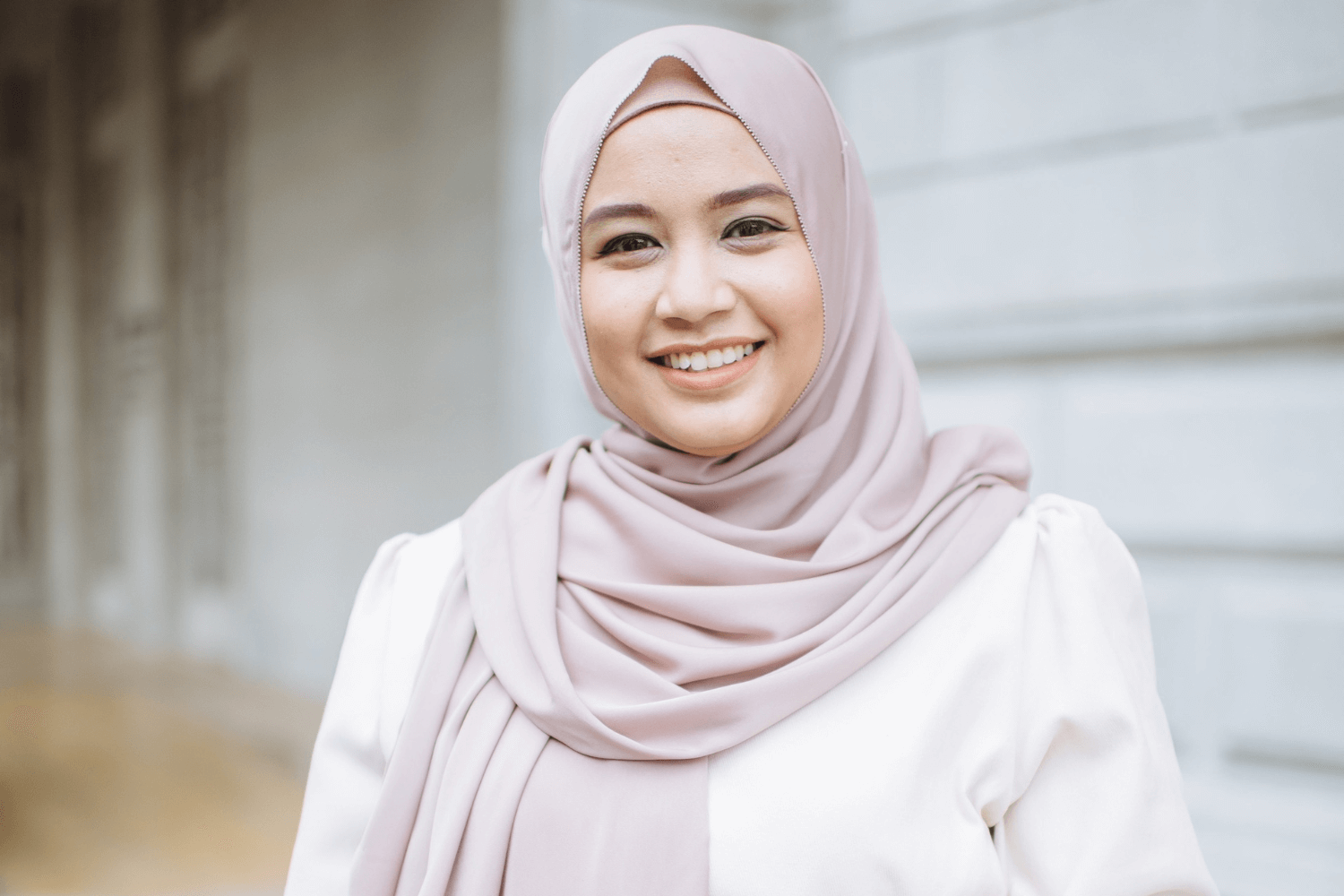 Une femme avec un couvre-chef rose et un haut blanc à manches longues, avec un jean. 