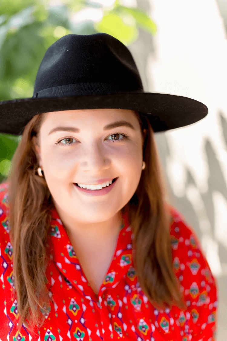 Une femme portant une chemise rouge à motifs et un chapeau noir à larges bords.