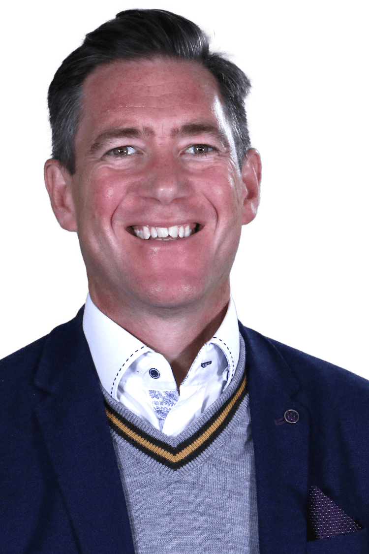 Un homme portant un blazer foncé, un pull gris et une chemise blanche