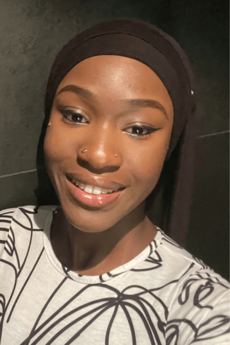 Une jeune fille portant un bandeau noir. Elle porte un chemisier blanc avec un motif linéaire noir. 