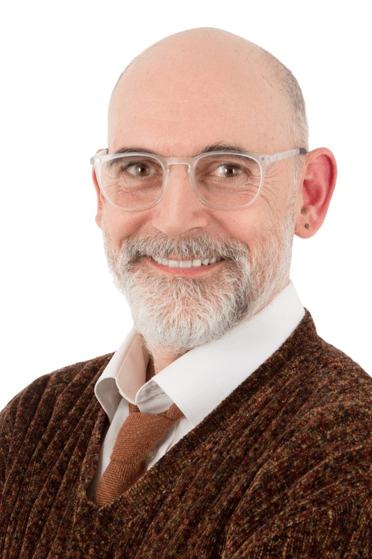 Un homme barbu avec des lunettes. Il porte un pull marron, une chemise blanche et une cravate.