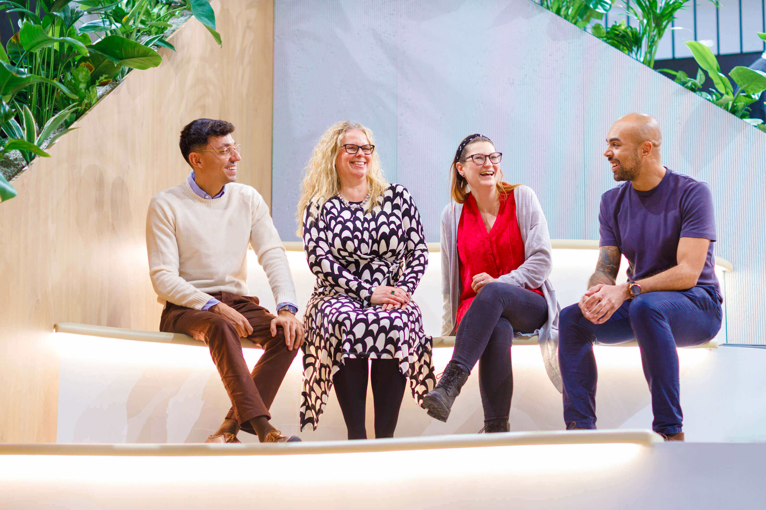 Een groep van vier mensen zit samen te lachen op een trapje. Er zijn twee mannen en twee vrouwen.