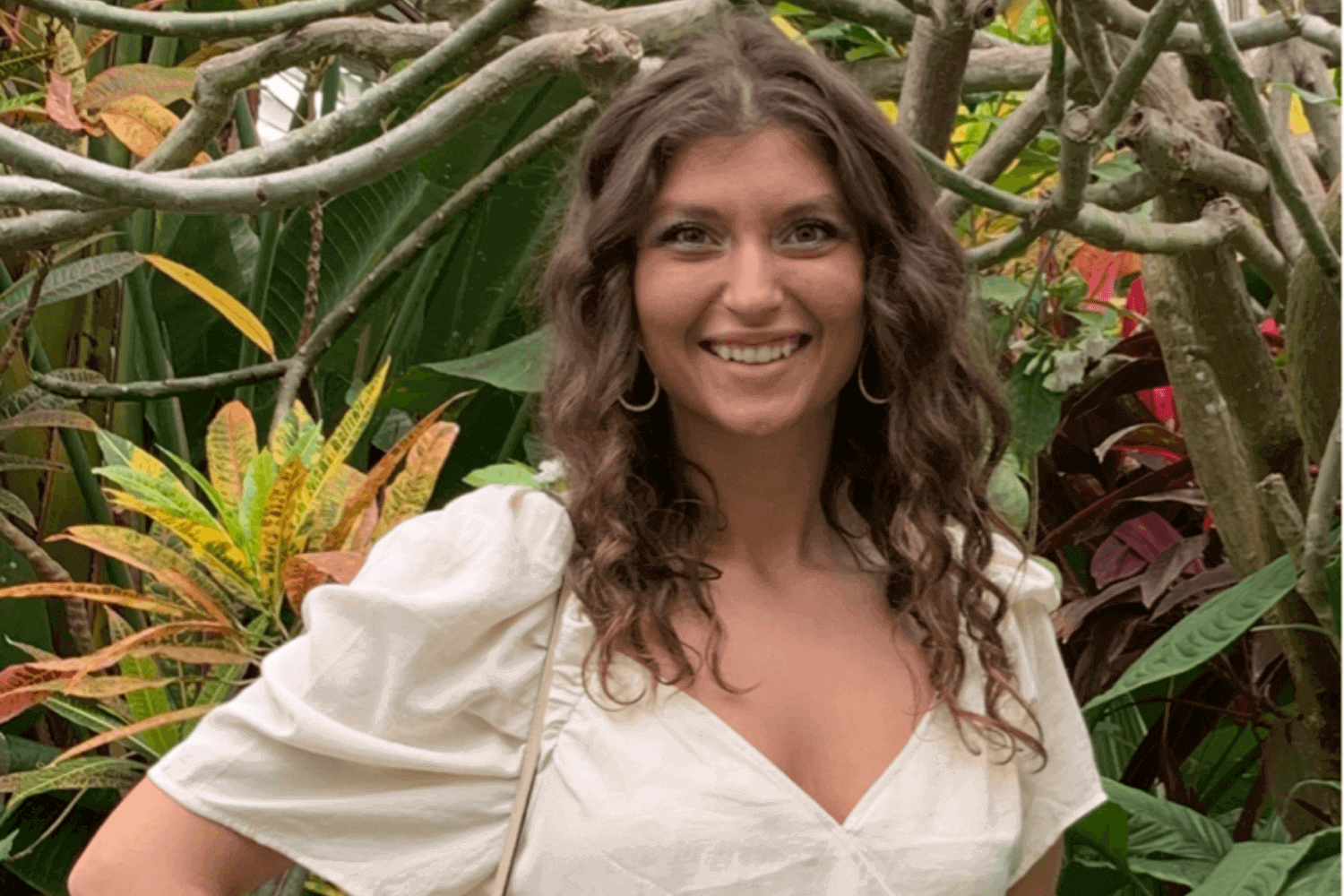 Een vrouw in een witte top met korte mouwen en een spijkerbroek. Ze is omringd door planten.