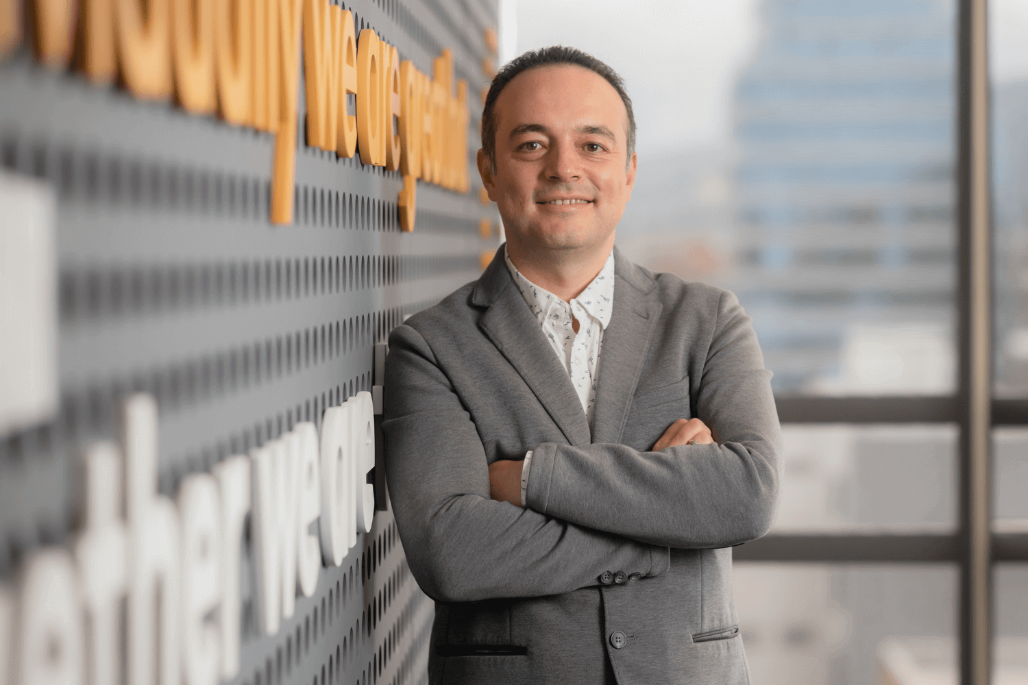 Een man leunt tegen een muur. Hij draagt een grijs jack met wit overhemd. 