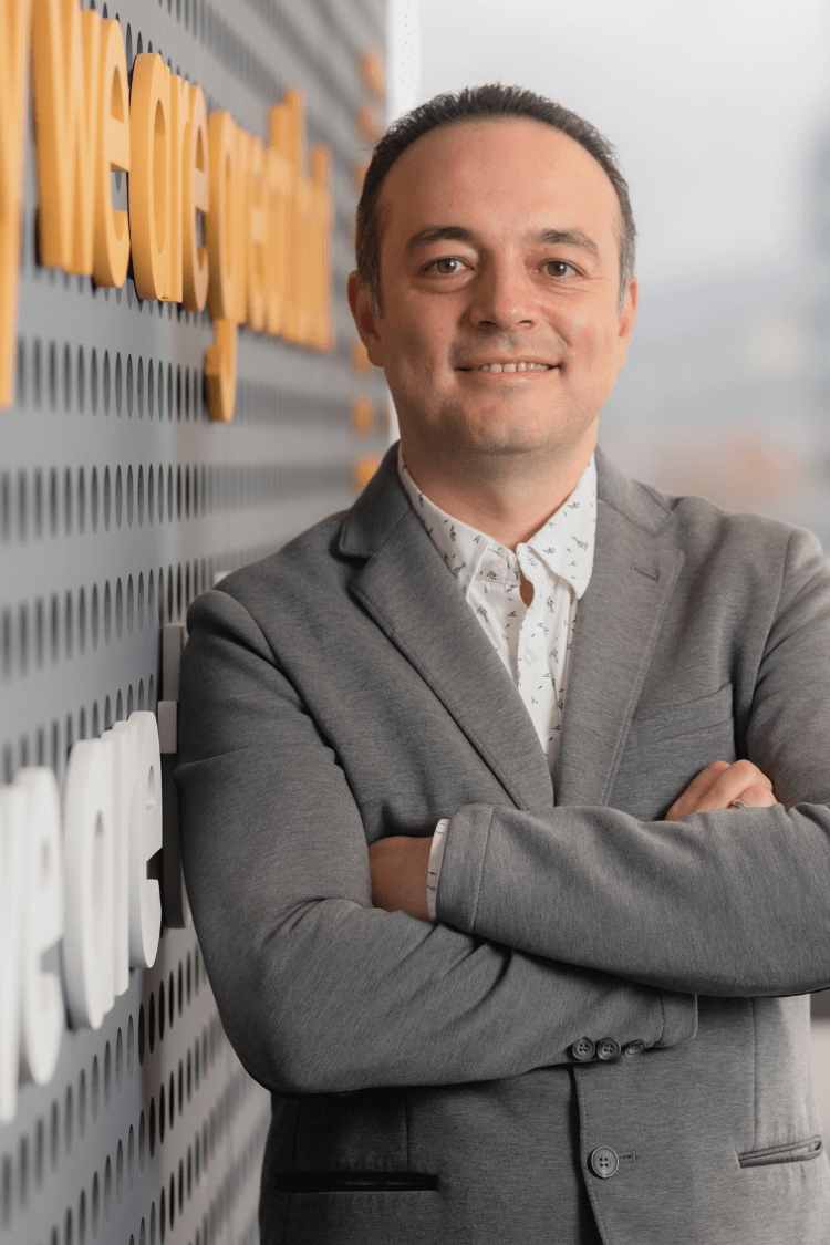 Een man leunt tegen een muur. Hij draagt een grijs jack met wit overhemd. 