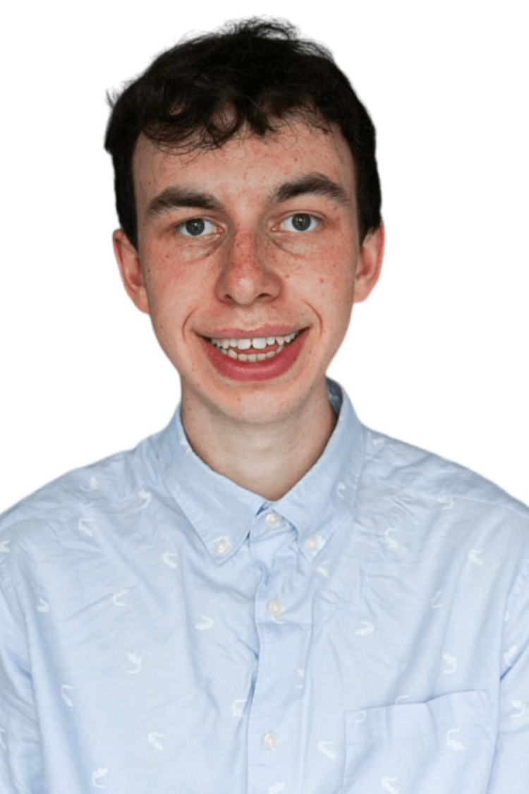 Een jonge man met kort krullend haar. Hij draagt een blauw overhemd met knoopjes. 