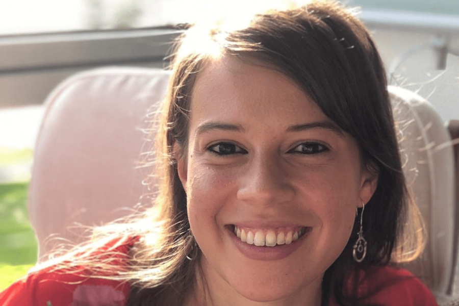 一位深色头发略长于肩的女性,身穿红色花纹上衣,对着镜头微笑。