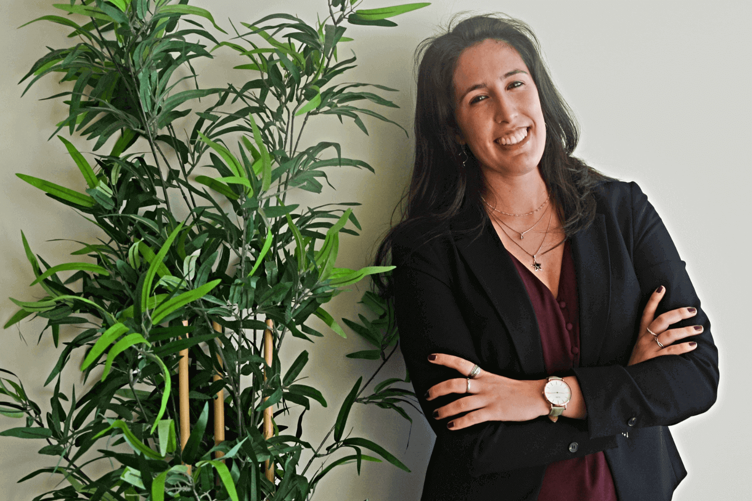 一位妇女倚靠在一株植物旁。她留着棕色长发，身穿黑色外套和红色连衣裙。