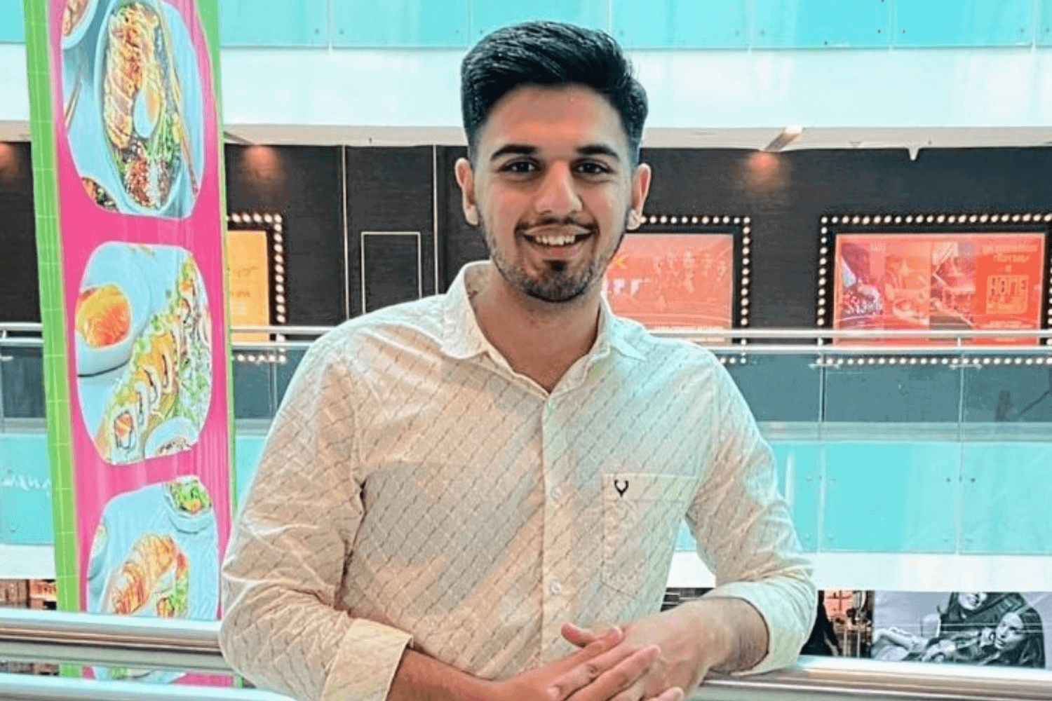 一名身穿白衬衫和牛仔裤的男子站在购物中心的阳台栏杆旁。